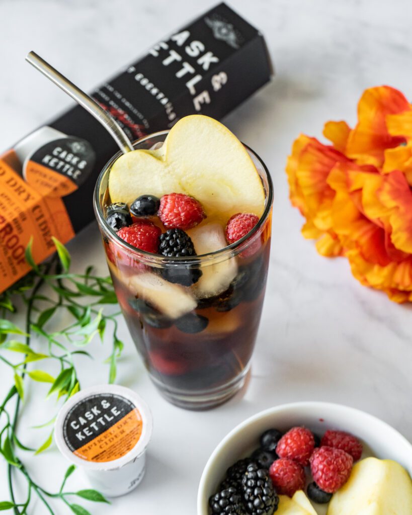 Sangria and fruit in a tall clear glass with fruit garnish nearby